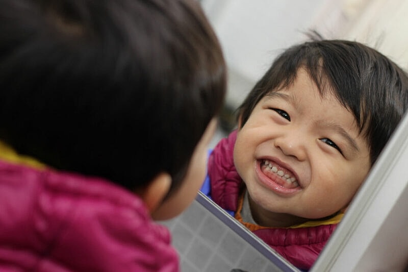Child smiling in mirror, joyful expression.