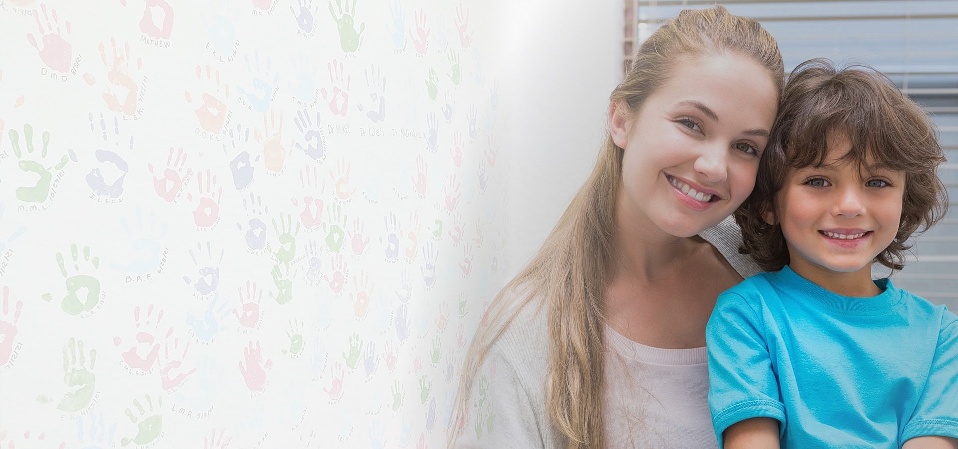 Smiling woman with child against colorful handprint wall.